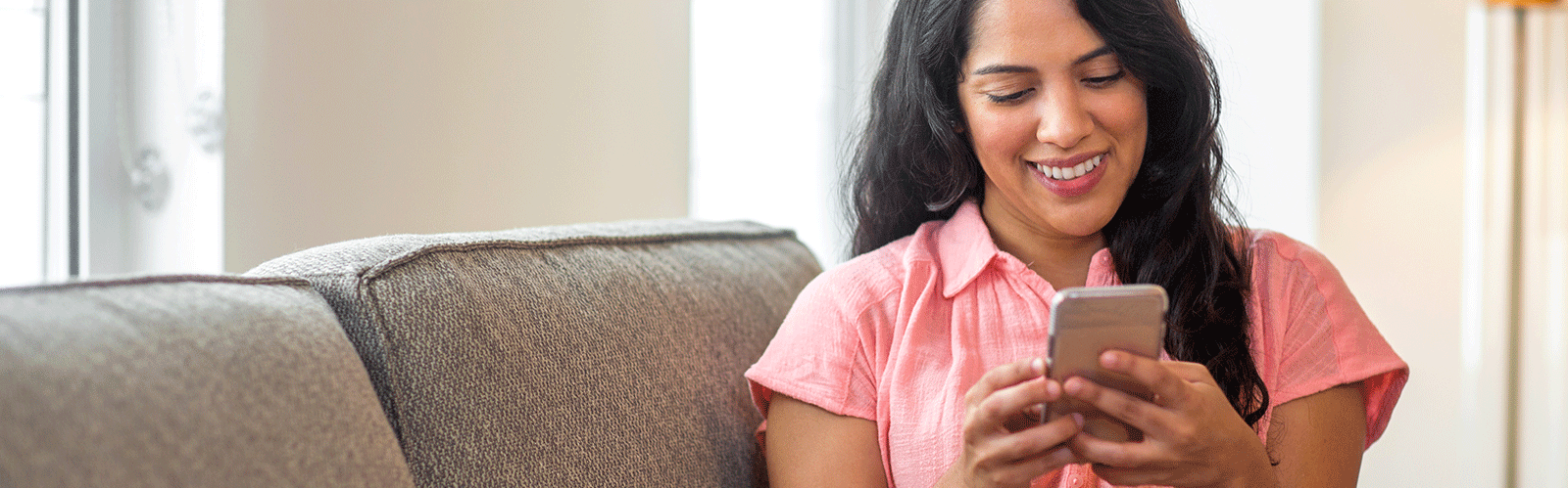 woman in pink shirt smiling and looking at phone