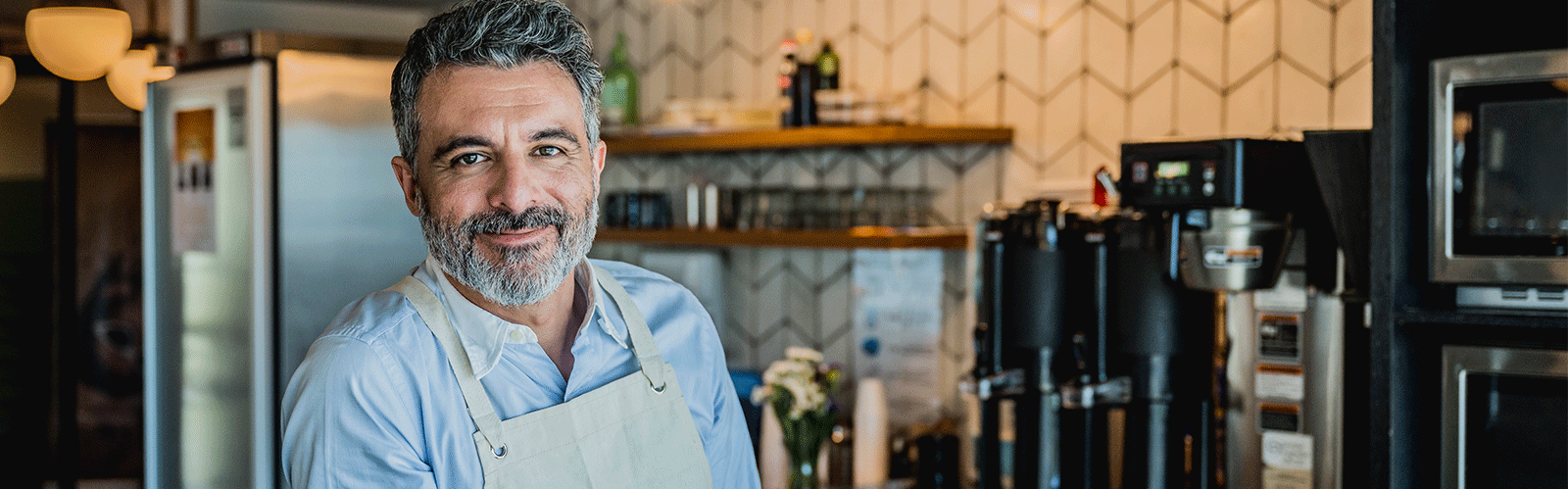 man wearing apron smiling at camera with kitchen in background