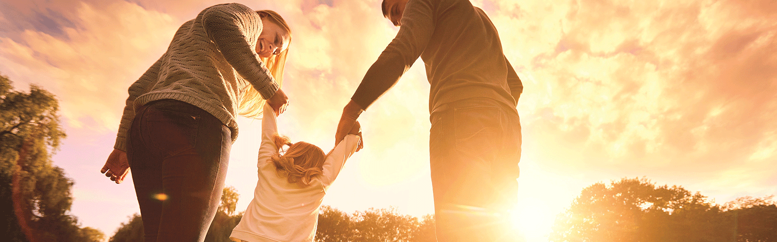 mom and dad swinging young daughter by arms during sunset