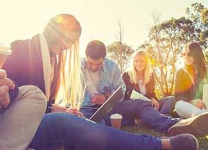 Group of teenagers sitting on grass on their computers.