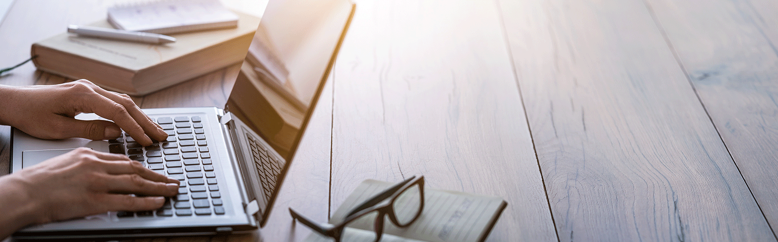 person typing on laptop with glasses and books next to it