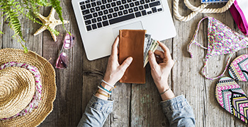 Person holding wallet with cash in front of laptop