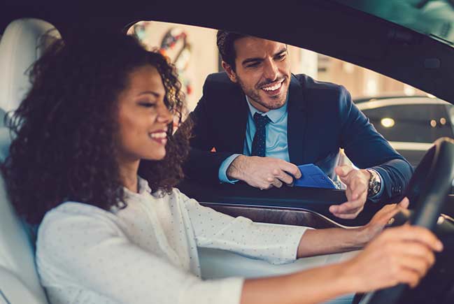 Car salesman talking to lady in car.