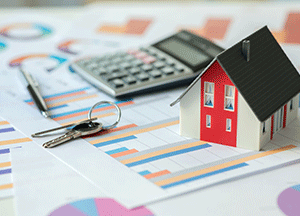 small toy home by calculator, keys, and a pen on papers